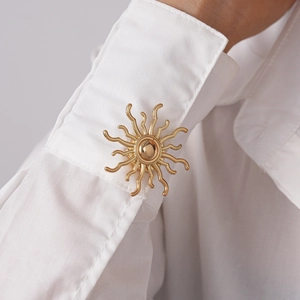 Detailed view of a golden sun flower cufflink on a white shirt sleeve with metallic shine