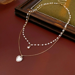 Détail d'un collier double rang doré avec pendentif cœur, perles et zircone élégant