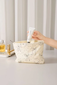 Close-up of beige canvas makeup bag with black bow print and hand taking out skincare