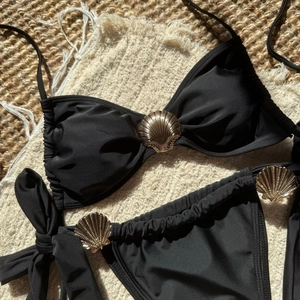 Detail of black bikini set featuring golden shell ornaments on textured beach mat