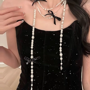 Long faux pearl necklace featuring black glitter bow accents in an elegant layered style
