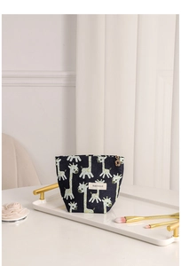 Detail of navy blue giraffe jacquard cosmetic bag with flower charm on a white tray