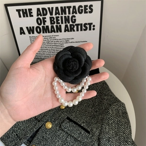 Detail of elegant black camellia brooch with white pearl tassels on tweed fabric