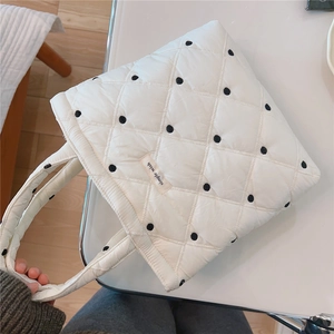 Close-up of white quilted handbag featuring black polka dots and twin handles