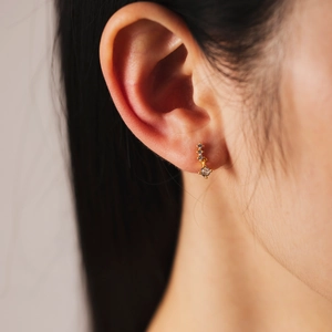 Close-up of golden S925 silver stud earrings with clear zircons in wavy design