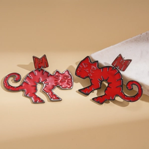 Detailed view of red enamel cat earrings with gold bow accents on marble background