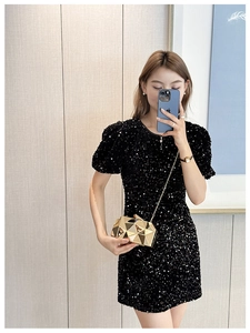 Detail of a gold geometric clutch bag with metal chain on a black sequin dress