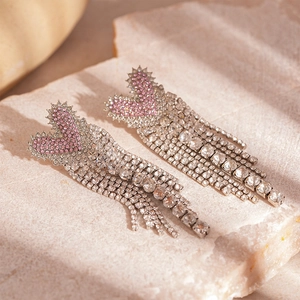 Macro shot of silver-tone drop earrings with pink rhinestones and tassels on stone
