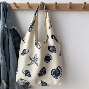 Detail of canvas tote bag with navy sea shell prints hanging on a wooden hook