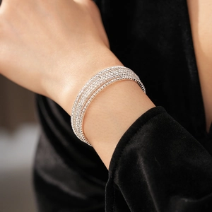 Close-up of a multi-layer silver rhinestone bracelet worn on a wrist over dark velvet