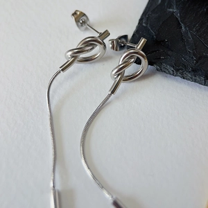 Close-up of silver knot tassel earrings on a natural black stone against white background