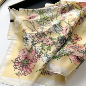 Close-up of a square silk scarf with yellow base and pink floral butterfly patterns in a tray