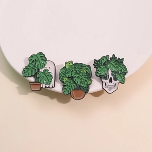 Three-piece monstera plant enamel pin set with ghost, frog, and skull badge designs