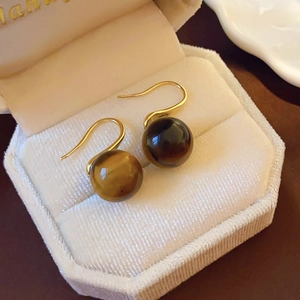 Macro detail of brown tiger eye earrings inside a beige velvet hexagonal jewelry box