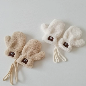 Close-up of plush fleece baby mittens with cute bear embroidery in beige and white