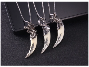 Detail of silver wolf tooth necklaces with engraved wolf, elephant, and tiger head charms