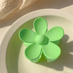 Close-up of green matte floral hair claw clip on a white plate with soft shadows