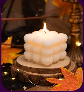 Macro shot of a white pumpkin cube candle with maple leaves and warm fairy lights