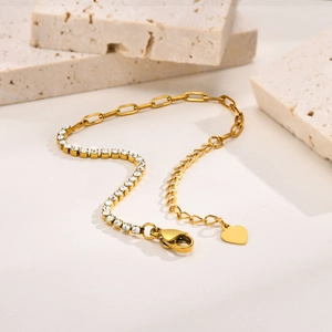 Detail of gold chain bracelet with square cubic zirconia and heart pendant on stone