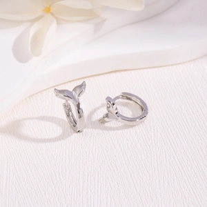 Macro shot of silver mermaid tail earrings on a textured white floral background