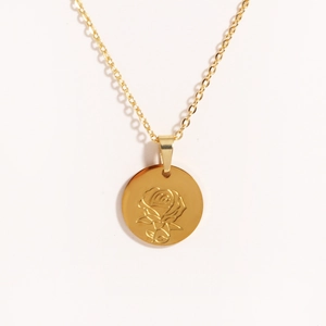 Macro detail of a gold oval pendant featuring an etched rose on polished titanium steel