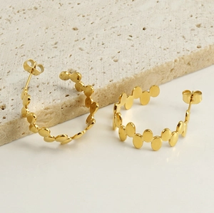 Detailed close-up of C-shaped 18k gold earrings with wavy disc texture on stone