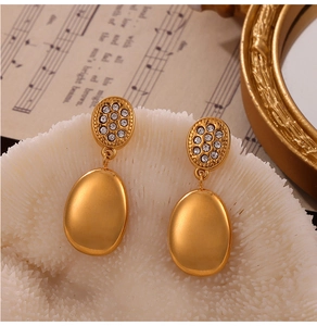 Detailed close-up of gold drop earrings with micro-diamonds on a white coral surface