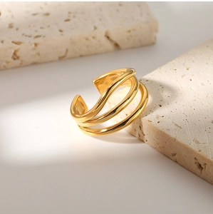 Detailed view of multilayer 18K gold-plated wave ring on a textured beige travertine stone