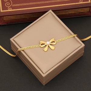 Detailed shot of golden pearl bow bracelet with flat snake chain on elegant jewelry box