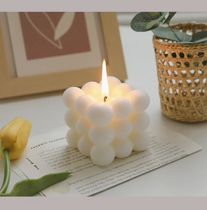 Close-up of a lit white cube bubble candle with a yellow tulip and vintage book