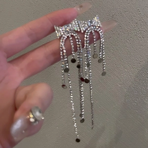 Close-up of sparkling rhinestone tassel bow earrings held in hand against grey background