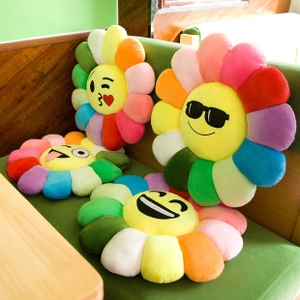 Group of colorful rainbow daisy flower cushions with various emoji faces on a sofa