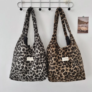 Detail showing plush leopard print tote bags in grey and brown hanging on a white wall