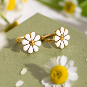 Detailed macro view of 18k gold-plated daisy flower earrings with white enamel on olive background
