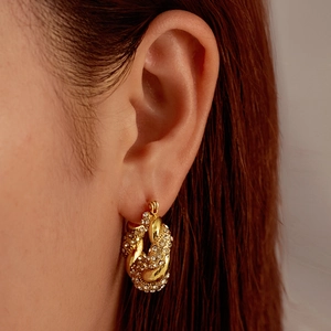 Élégante créole torsadée dorée ornée de strass brillants portée par un mannequin