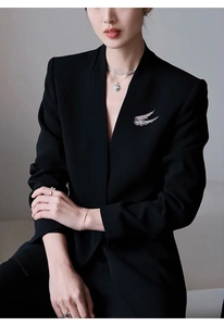 Detailed close-up of a silver angel wing brooch with sparkling rhinestones on a black blazer