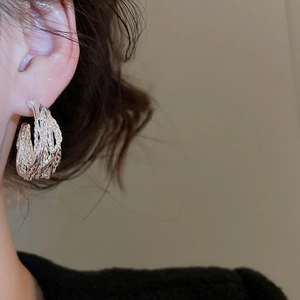 Detail of silver twisted weave earring worn by a model in a minimalist style