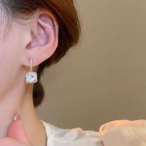 Close-up of elegant gold plated square zirconia earrings worn by a model in warm light