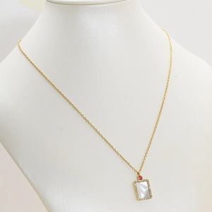 Detail of gold shell pendant necklace with pink gem on a white mannequin bust