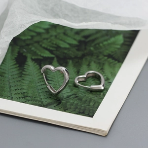 Close-up of silver heart-shaped hoop earrings displayed on a botanical card background