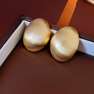 Détail macro de boucles d'oreilles ovales en or brossé dans un écrin de luxe marron
