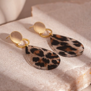 Macro detail of leopard print waterdrop earrings with golden studs on natural stone