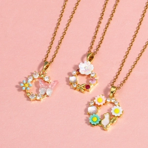Trois colliers dorés avec pendentifs papillon, couronne de fleurs et lapin sur fond rose