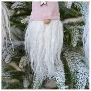 Close-up of pink plush Christmas gnome pendant with white beard and star on pine branch