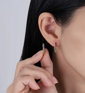 Macro detail of U-shaped gold earrings with blue and green rainbow zircons on ear