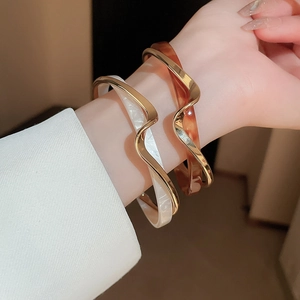 Detail view of wavy open bangles in gold with white shell and tortoiseshell patterns