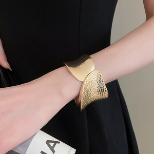 Detail of wide gold cuff bracelet featuring polished finish and hammered texture contrast