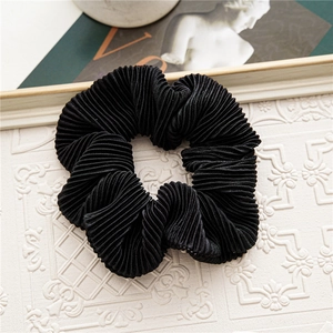 Detailed view of black pleated velvet scrunchie featuring elegant textured fabric ripples