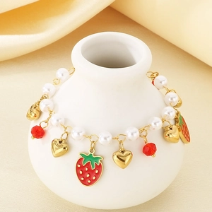 Detail of gold fruit charm bracelet with strawberry and pearl accents on ceramic vase