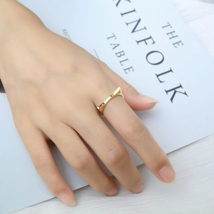 Detail shot of a gold cat-ear shaped minimalist ring worn on a finger over a magazine